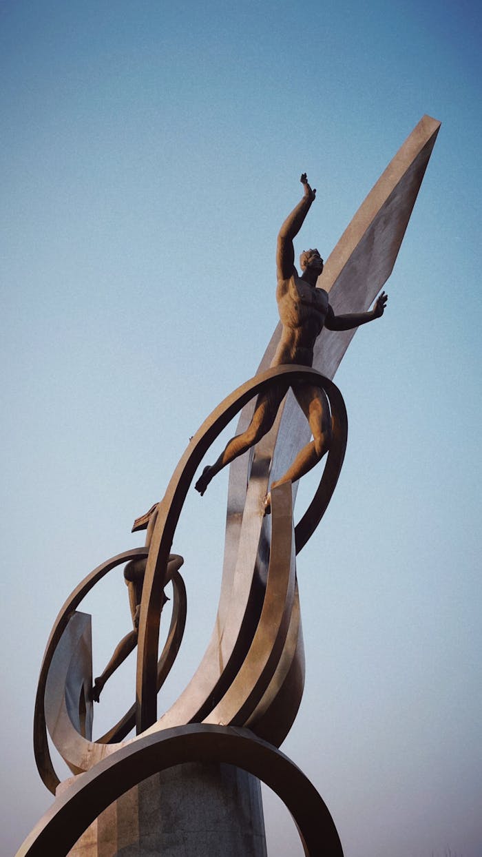 A modern sculpture depicting dynamic human figures against a blue sky.