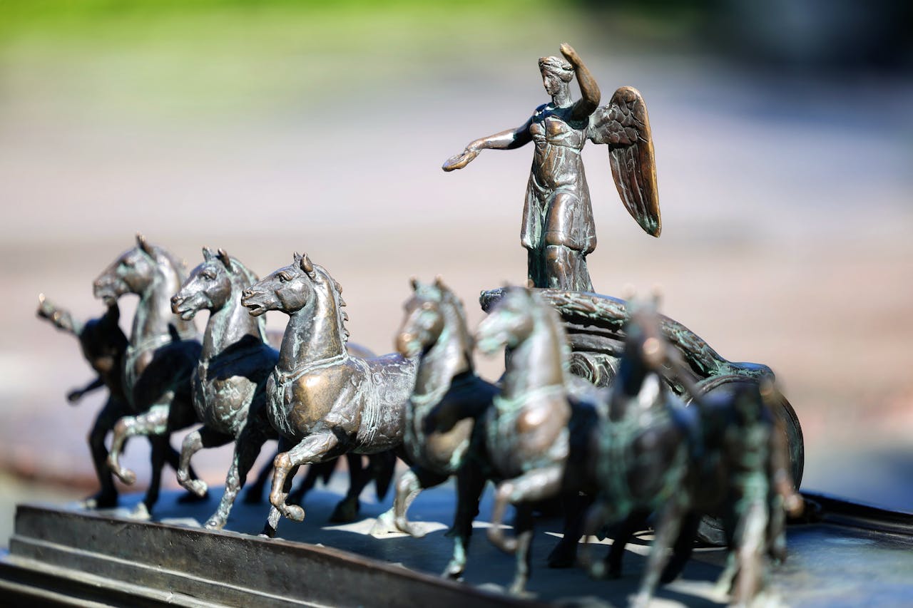 Detailed bronze sculpture of angel on chariot with horses, outdoor setting.
